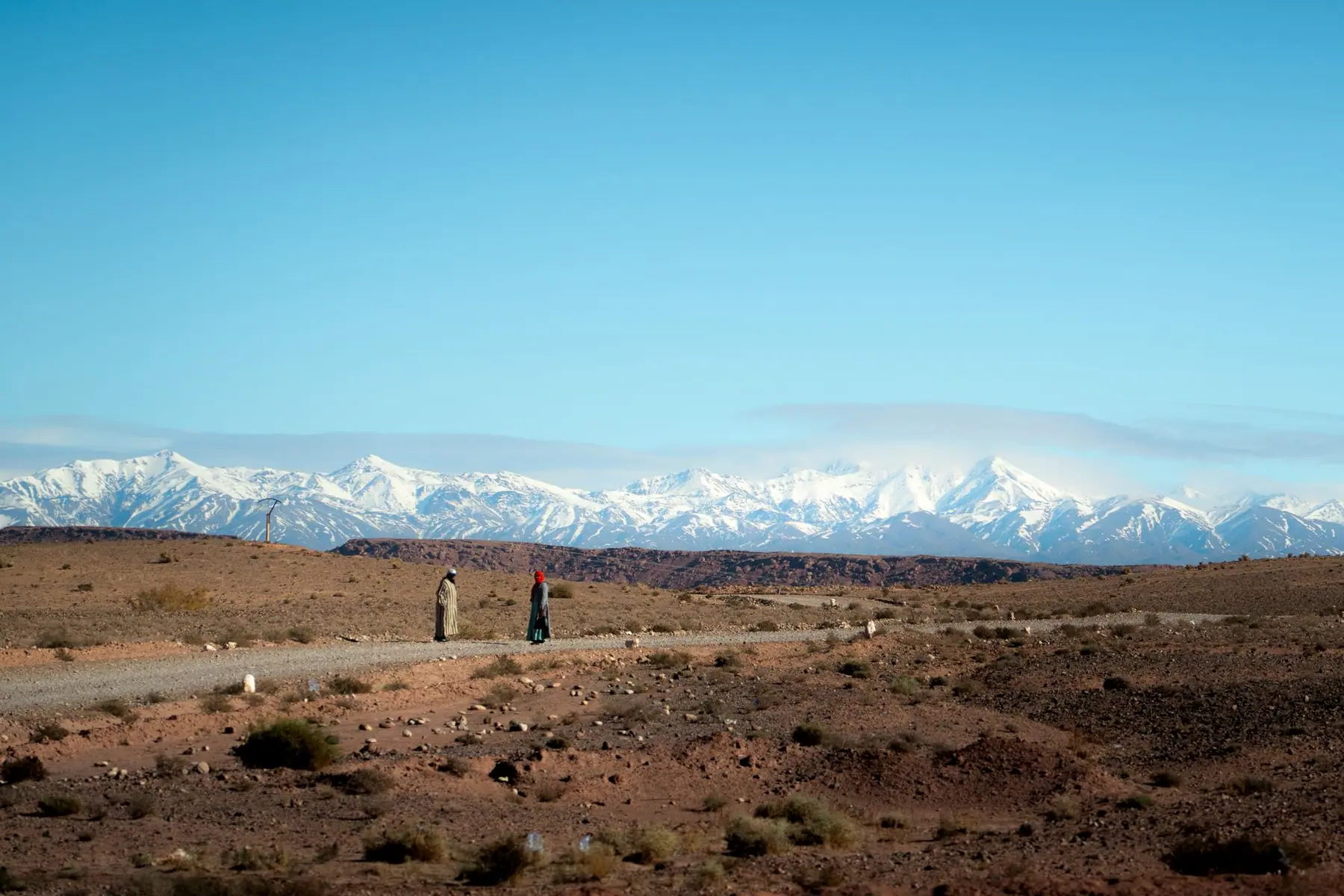 Deux personnes sur une piste, devant les sommets enneigés de l'Atlas.