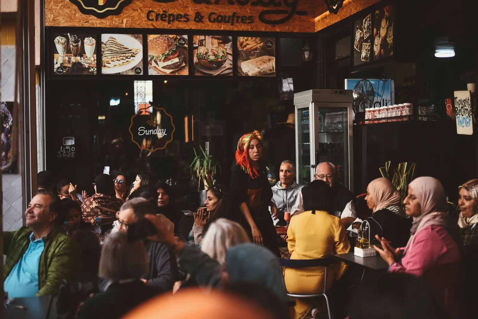 Salle animée d'un café à Agadir, des personnes assises autour des tables.