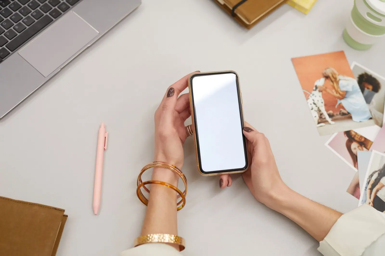 Deux mains tenant un téléphone à l'écran clair, à côté d'un ordinateur portable.